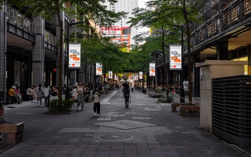 Rua arborizada de pedestres com painéis de mídia exterior ao longo da calçada, ilustrando o investimento em mídia por meio