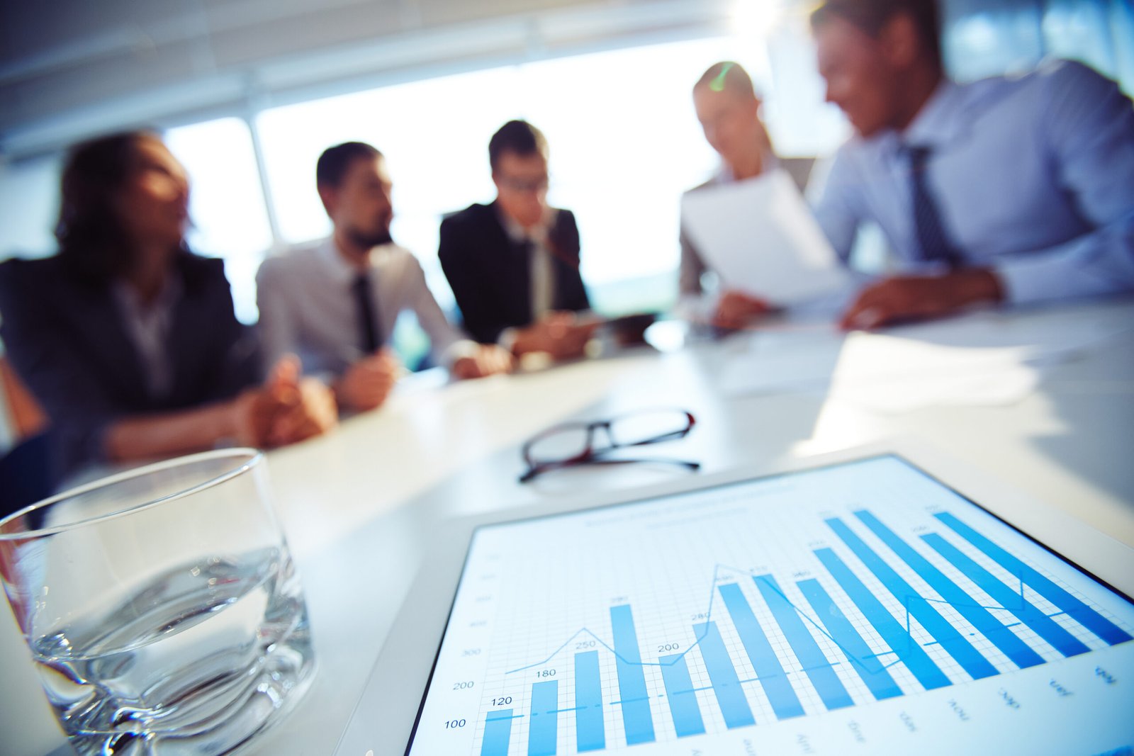 Pessoas em reunião ao redor de uma mesa com gráfico de barras impresso, sobre o planejamento de mídia de 2027