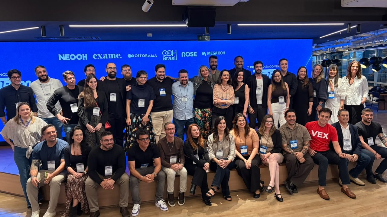 Grupo de profissionais reunido para foto em uma sala com painel de patrocinadores ao fundo